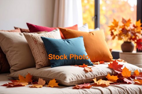 Cozy pillows in warm autumn colors are arranged on sofa, surrounded by vibrant fallen leaves, creating serene and inviting atmosphere perfect for season